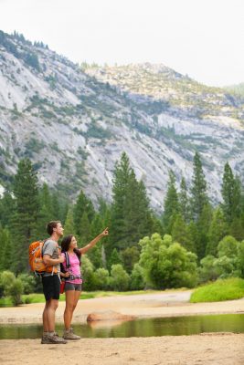Hiking people on hike in mountains in Yosemite. Hikers young couple pointing looking up in mountain landscape in Yosemite National Park, California, USA. Multicultural couple active outdoors.